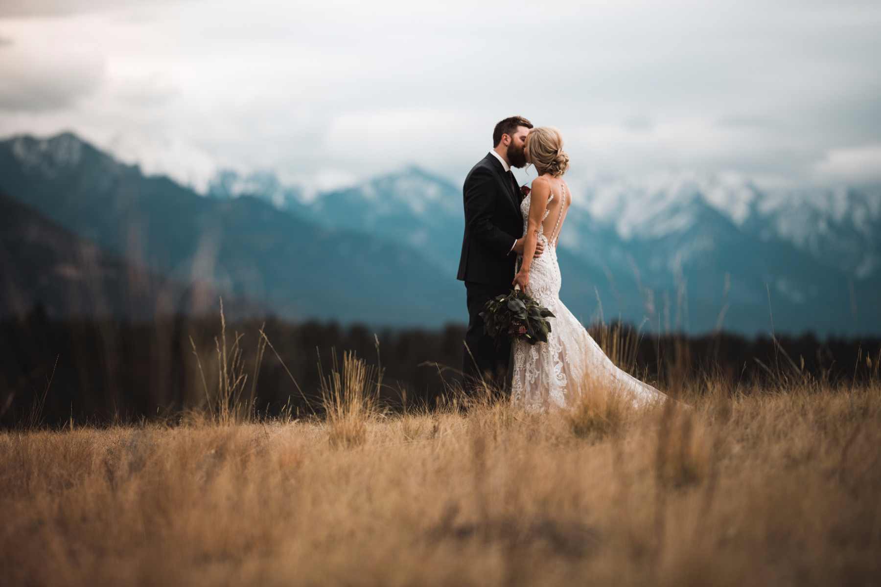 Calgary wedding photographer in Invermere for adventurous mountain destination elopement at Eagle Ranch Golf Resort, British Columbia - Newlyweds kissing in field with mountains